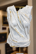 White draped female torso sculpture with gold leaf accents on brass display stand.