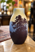 A ceramic vase with a hand-painted landscape design featuring dark pine tree silhouettes against a blue and cream gradient background, displayed on a polished stone countertop.