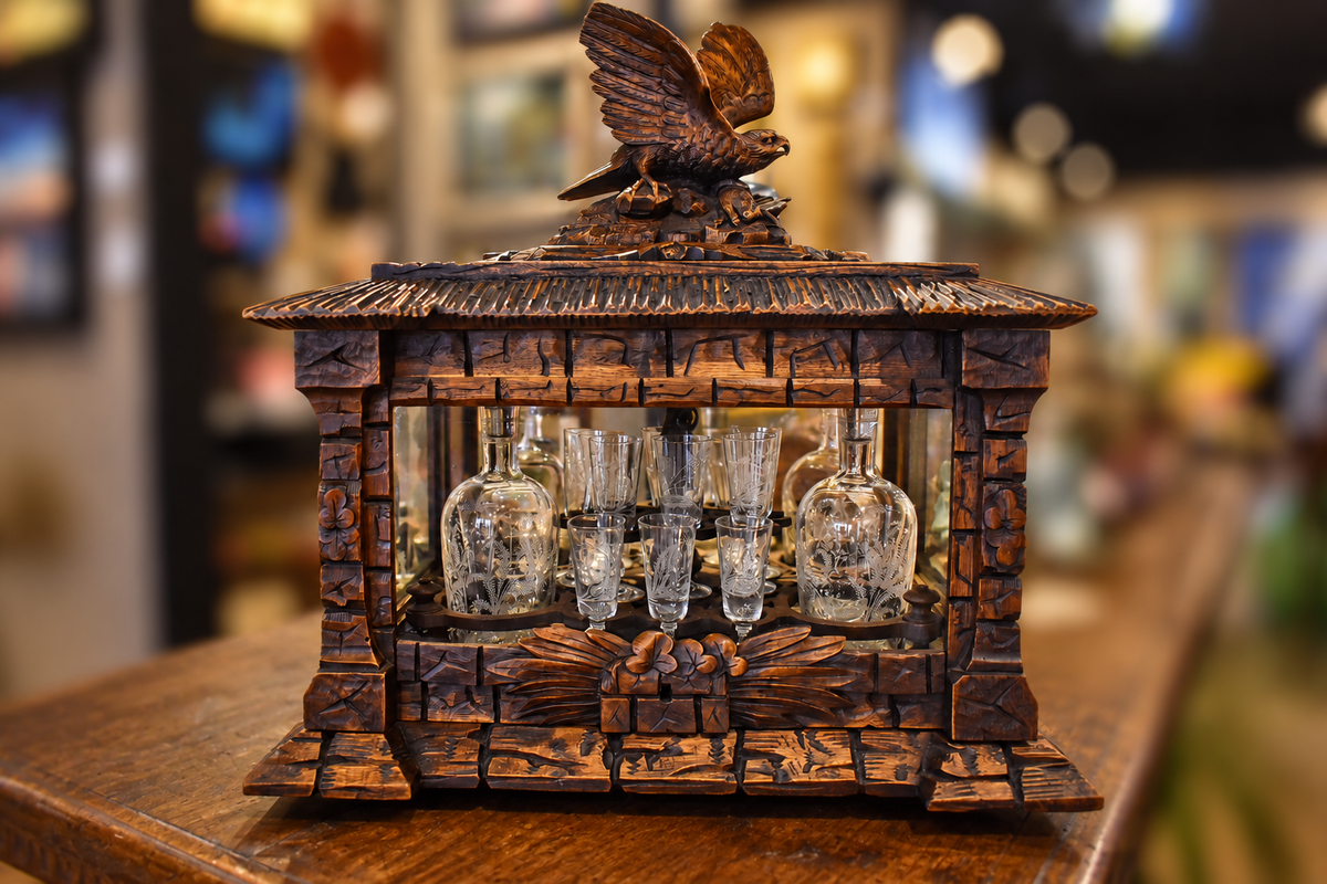 Carved oak Black Forest tantalus with a bird finial and displayed glass decanters and tumblers