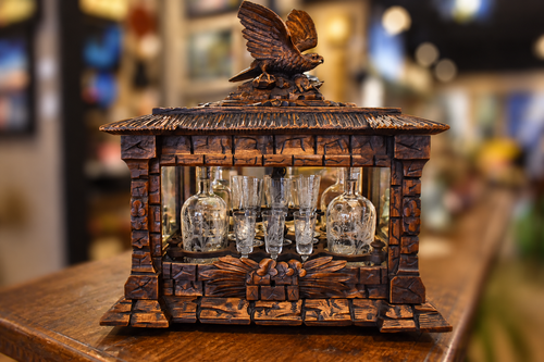 Carved oak Black Forest tantalus with a bird finial and displayed glass decanters and tumblers