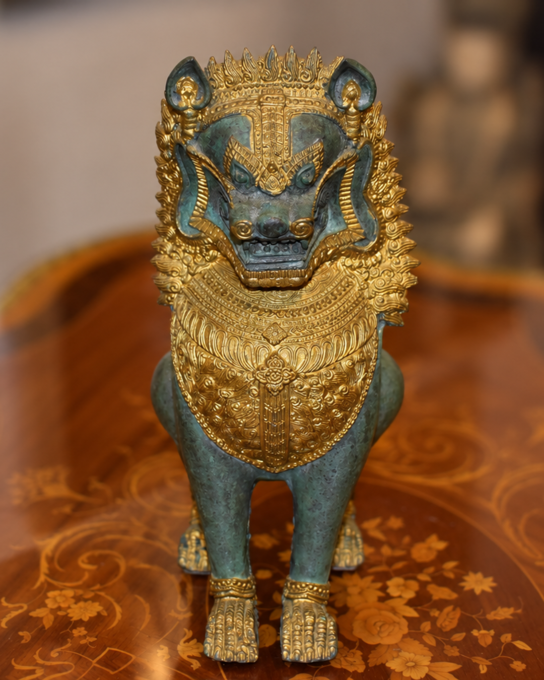 A decorative golden lion statue with a blue-green patina finish, standing on an ornate wooden surface.