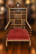 Front view of a Middle Eastern wood armchair with mother-of-pearl inlay, an intricately carved back, open arms, and a red upholstered seat
