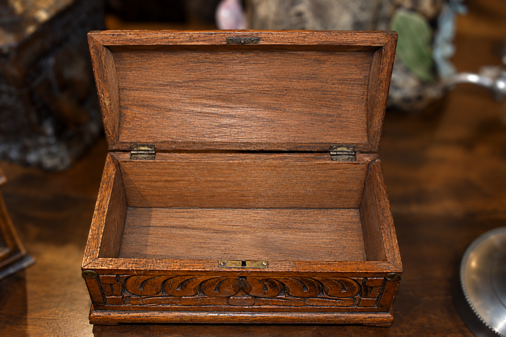 Hand-carved oak jewelry box shown open, revealing an unlined wooden interior, hinged lid, and carved floral decoration across the front.