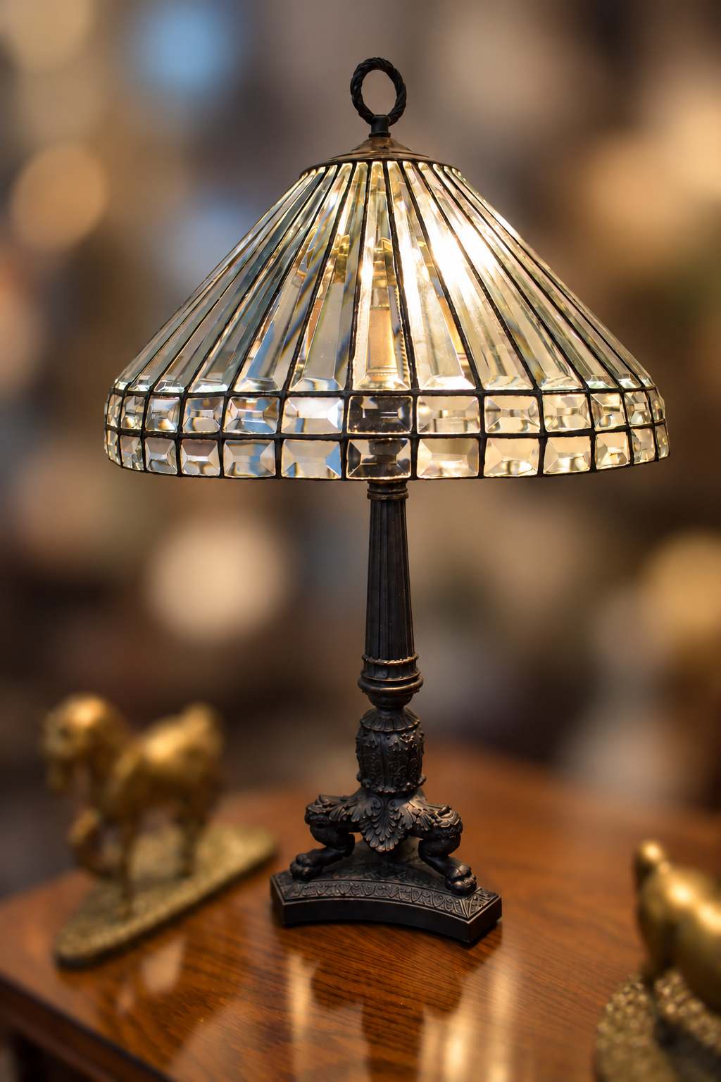 Leaded beveled glass table lamp with a wide conical shade and ornate dark metal base, illuminated on a wooden table