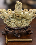 An ornate carved jade decorative object with a small figurine on top, set on a dark wooden stand, on a wooden surface.