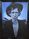A framed portrait painting of Keith Richards with blue skin, wearing a black hat and dark clothing, set against a blue background. The artwork is housed in a thick black frame.