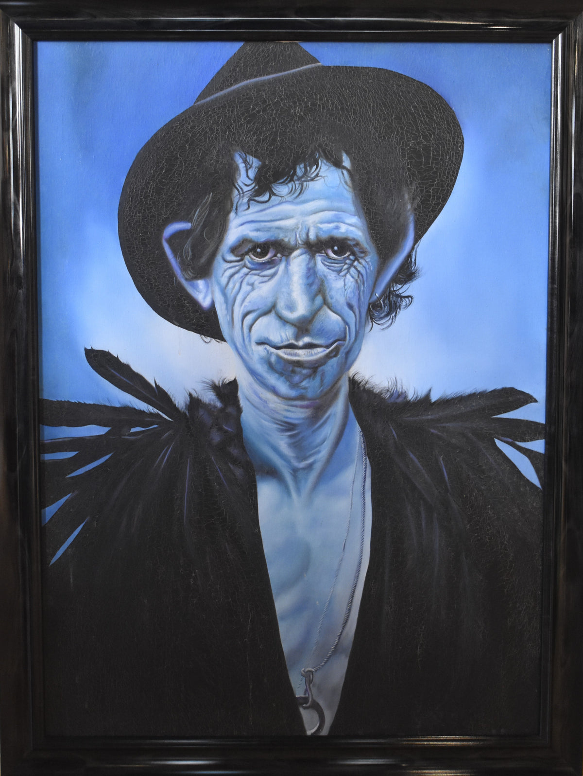 A framed portrait painting of Keith Richards with blue skin, wearing a black hat and dark clothing, set against a blue background. The artwork is housed in a thick black frame.