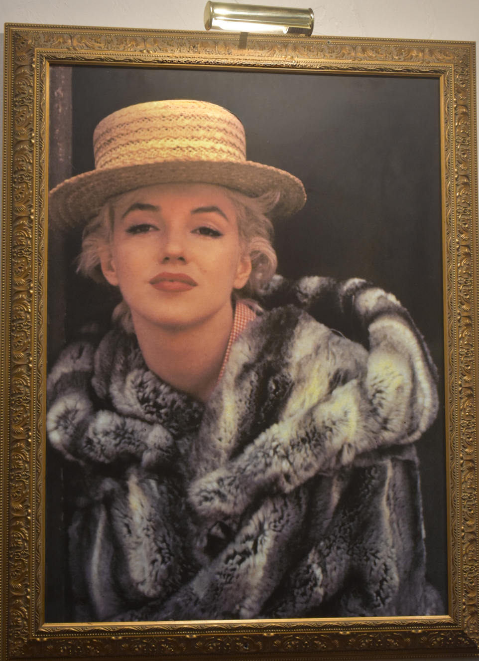 A framed portrait print of Marilyn Monroe wearing a straw hat and a fur coat, enclosed in an ornate gold frame.
