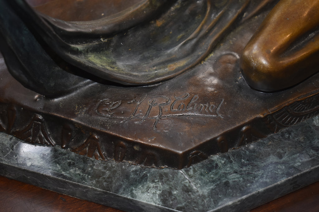 Close-up detail of a bronze sculpture base with an engraved signature and a polished metallic bronze figure on a dark stone pedestal.