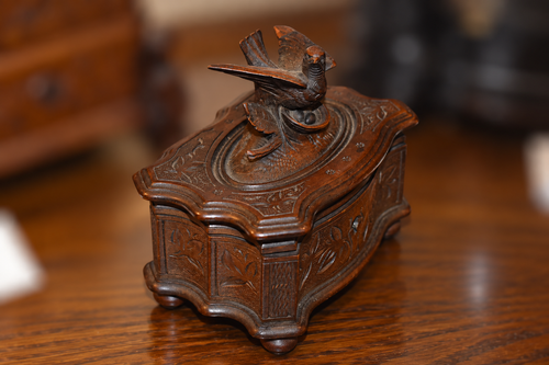 19th-century Black Forest carved walnut trinket box closed, showing serpentine bombe form with all-over foliate carving, spread-wing pheasant finial on lid, brass escutcheon, and bun feet