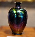 Iridescent glass vase with a rounded body, narrow neck, flared rim, and green, blue, violet, and amber highlights