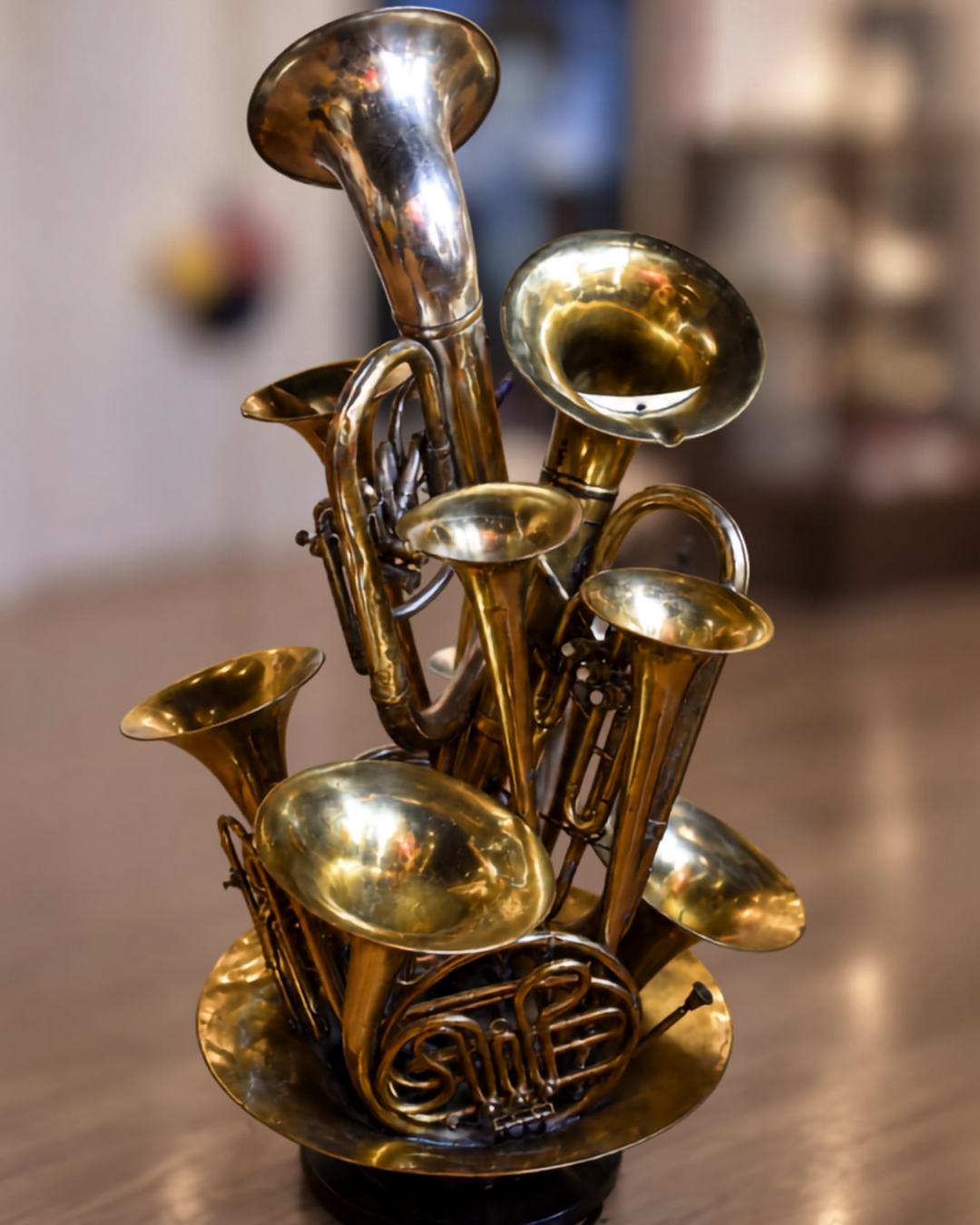 A decorative sculpture made from multiple brass instruments, including tubas, French horns, and trumpets, arranged together on a round base in a warm indoor setting.
