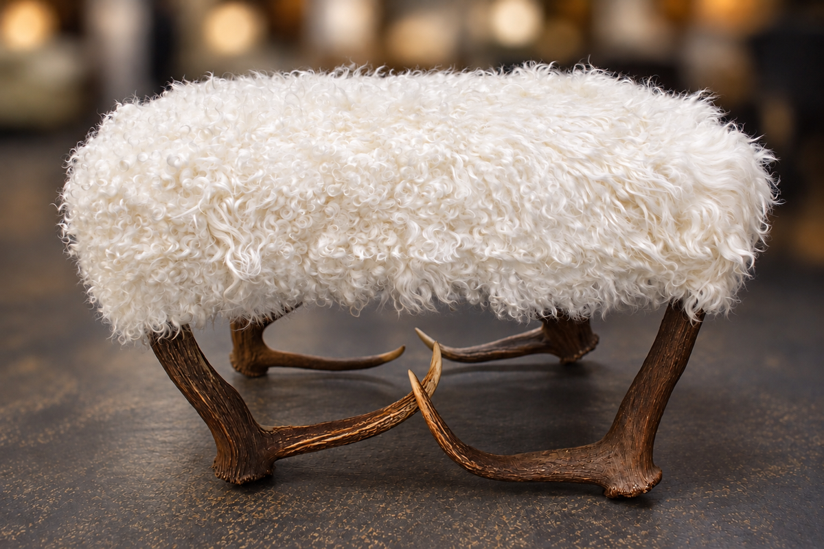 A rustic bench or stool with a thick, fluffy white sheepskin or faux fur seat and four natural brown antler legs, set against a dark textured background.